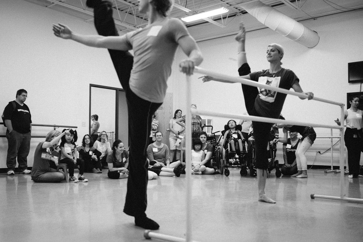 Dancers practicing high kicks in a mirrored studio during rehearsal.