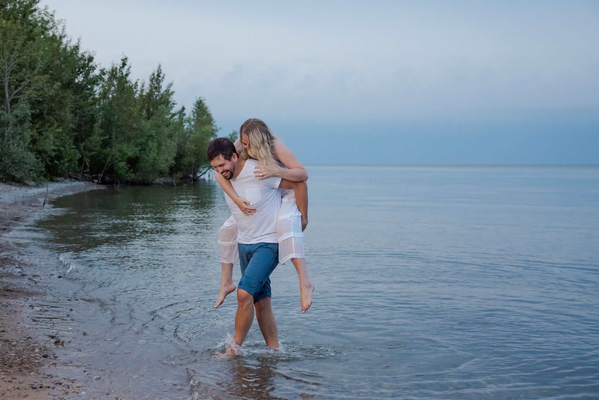 A couple shares a romantic moment while wading in the calm waters of a lake at dusk.