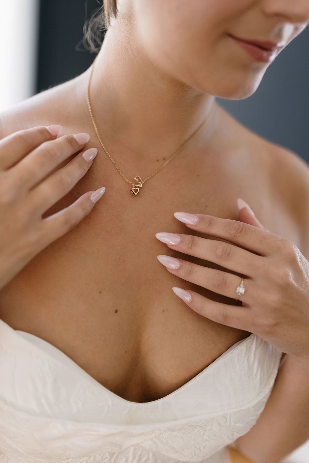 Close up shot of a delicate gold necklace worn with a white dress, showing elegant hand placement on collarbone.