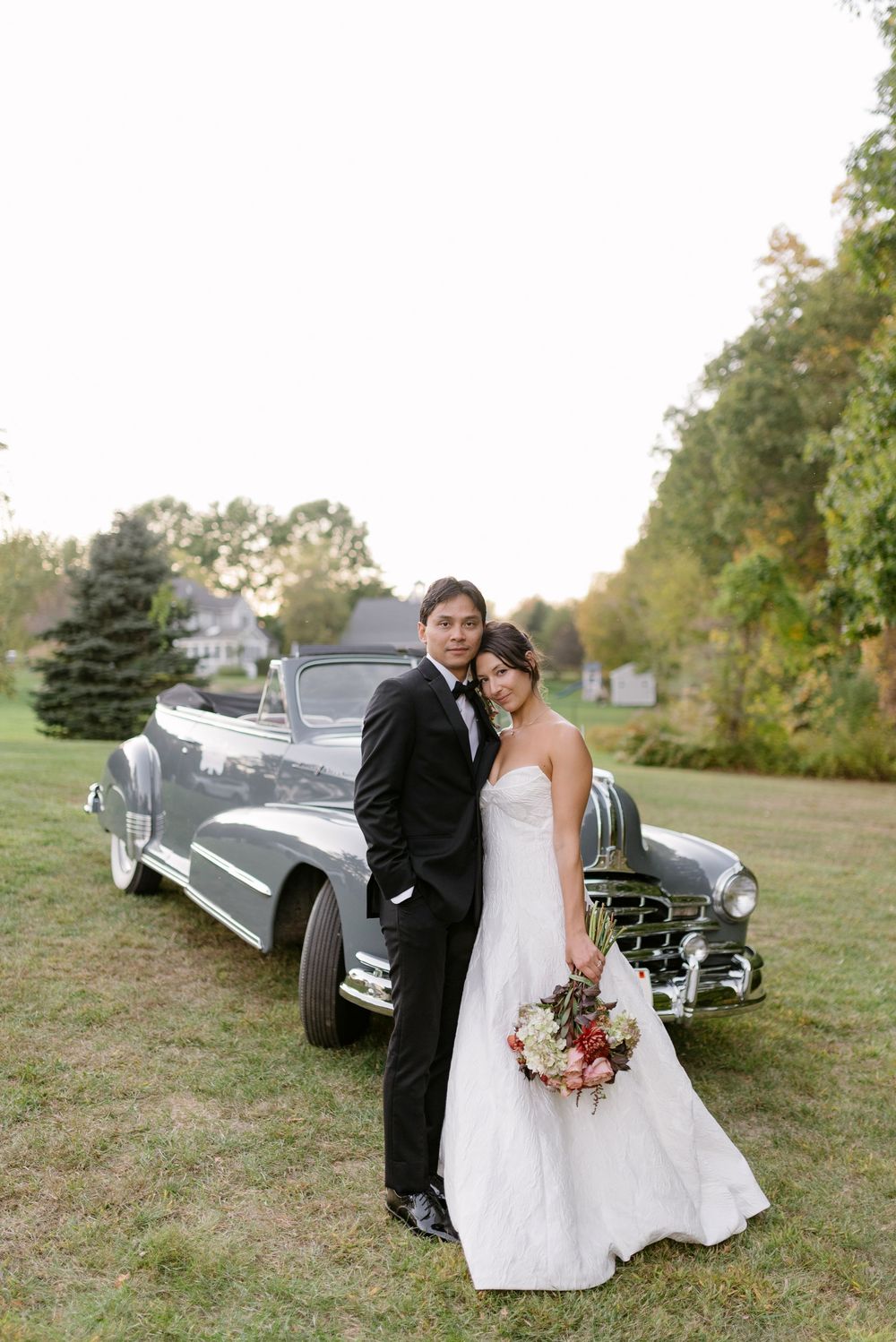 Vintage car parked on grassy hill during autumn wedding photoshoot.