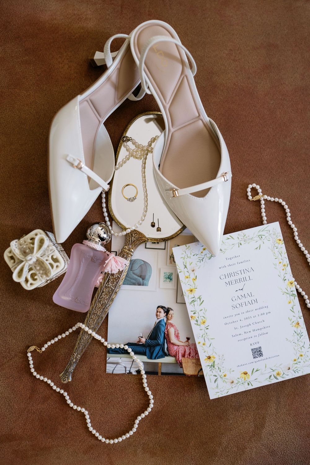 Wedding details including white bridal shoes, pearl necklace, and floral invitation cards arranged on brown textured background.