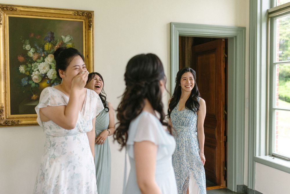 Bridesmaids in floral and blue dresses laughing together before a wedding ceremony in an elegant room.