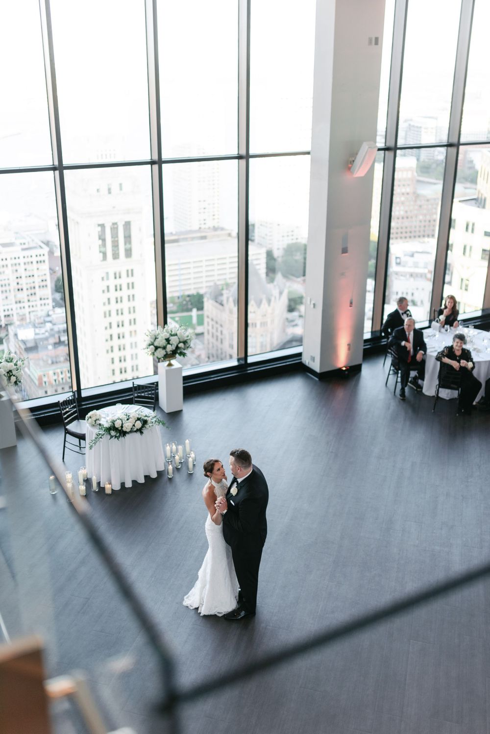 Bird's eye view of a wedding dance in a modern venue with floor-to-ceiling windows.