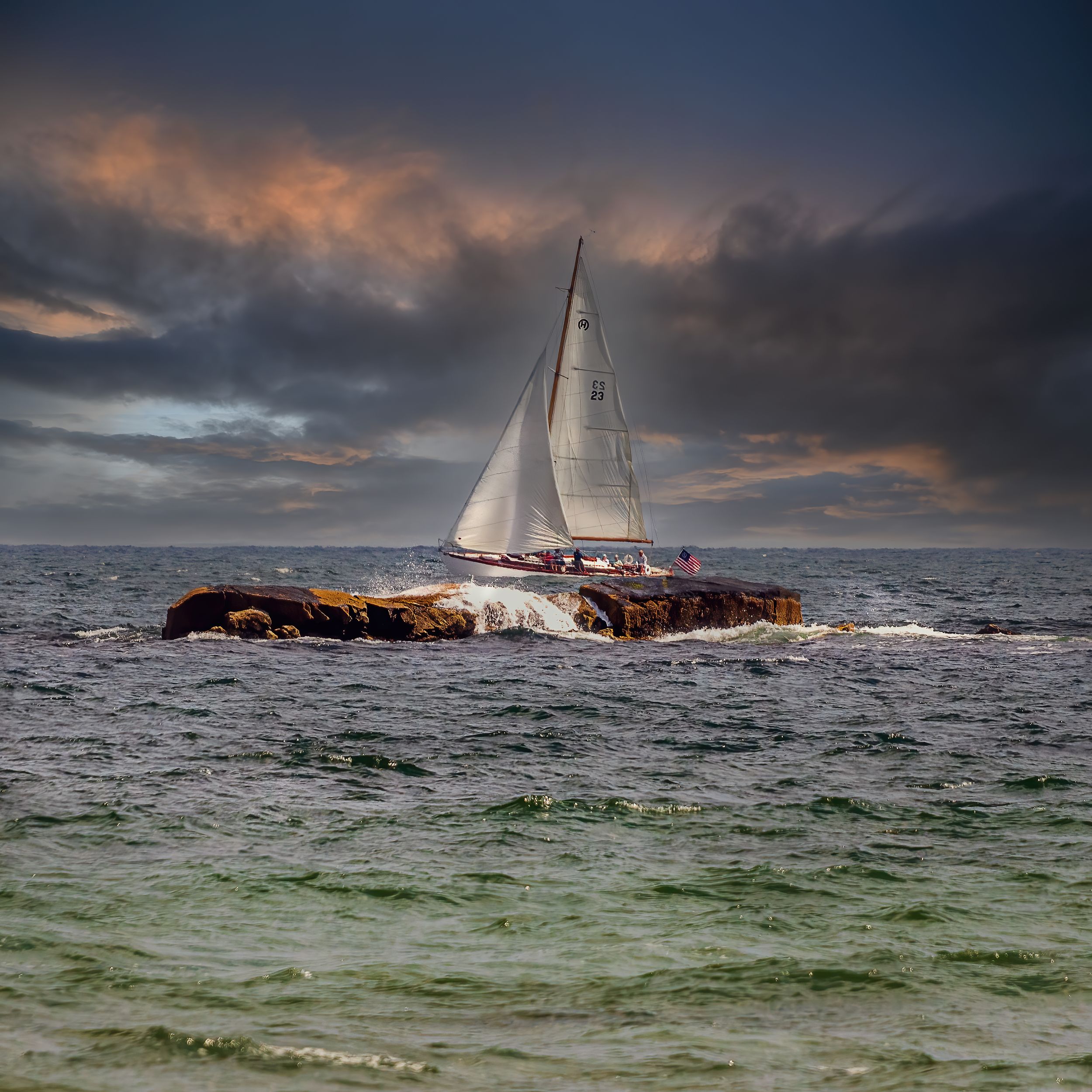 A sailboat navigates past rocky outcrops under dramatic stormy clouds during sunset on choppy ocean waters.
