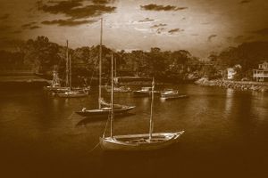 Sepia-toned photograph of sailboats anchored in a harbor at dusk with trees and buildings along the shoreline.