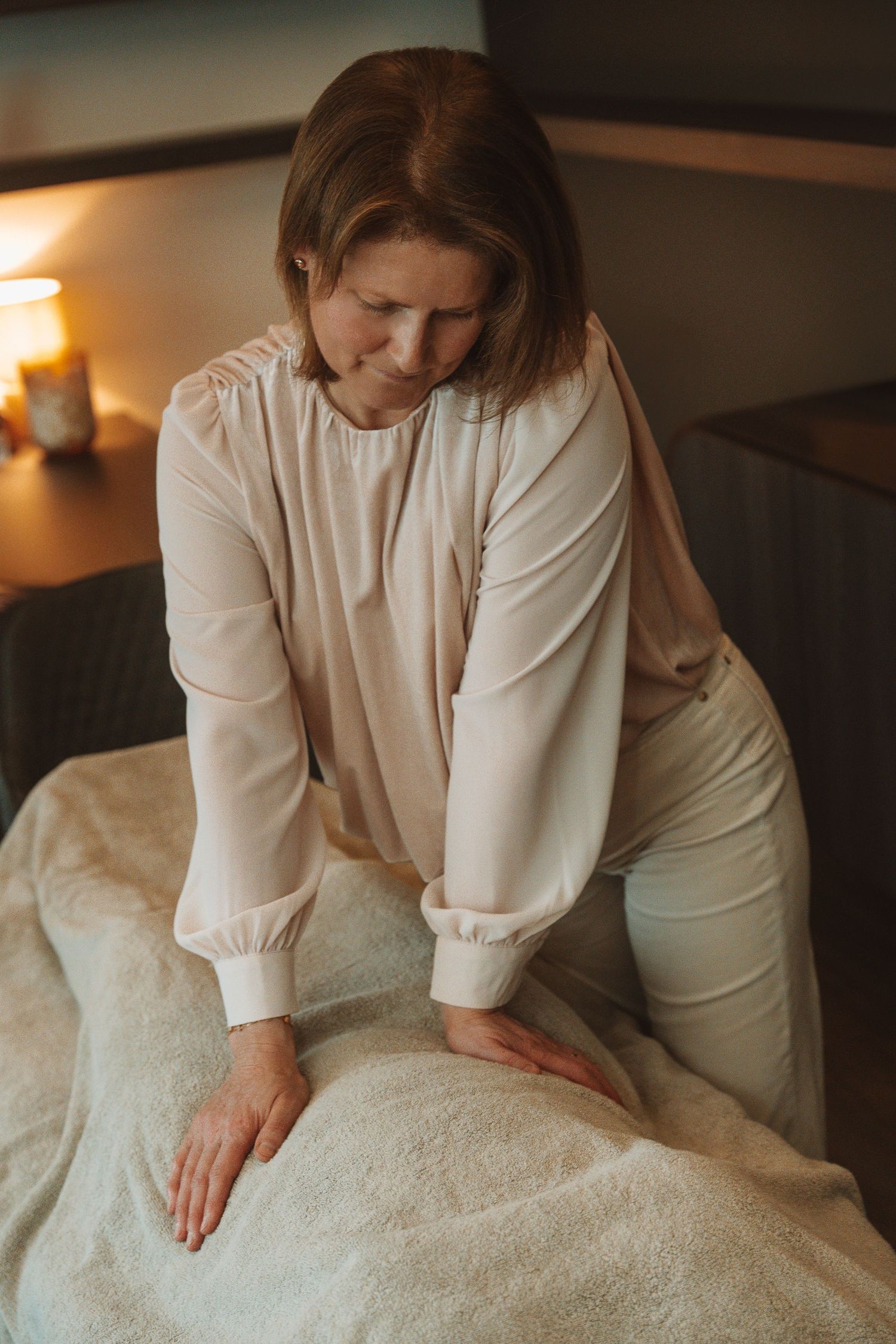 Professional massage therapist in white attire performs therapeutic massage treatment in dim, warm-lit spa setting.