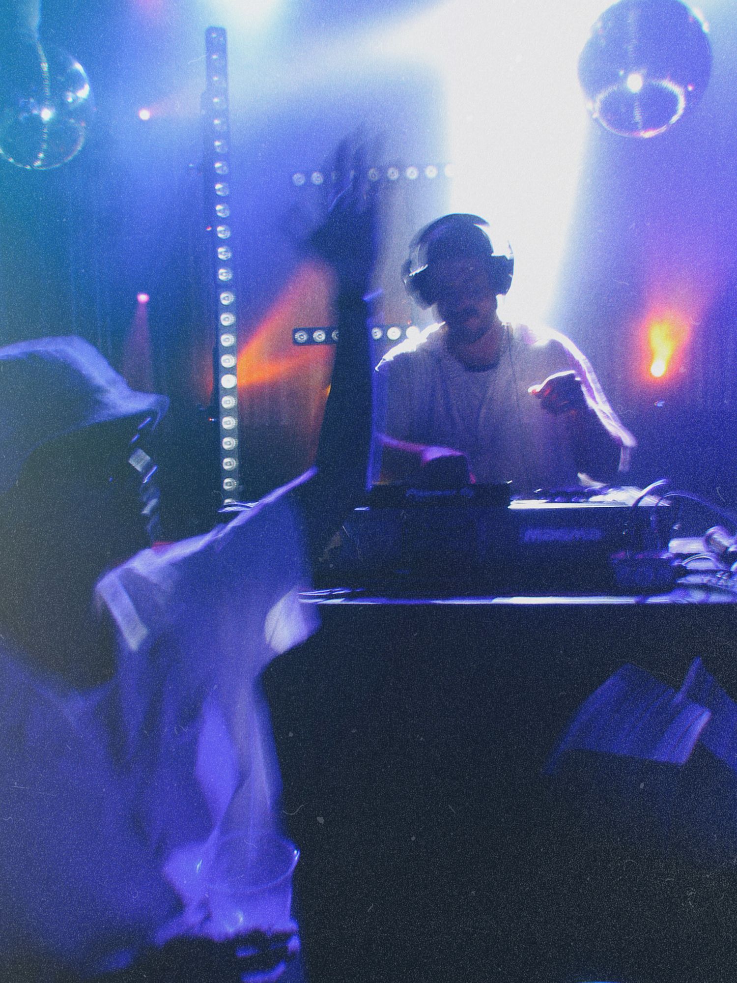 DJ performing in a moody nightclub setting with dramatic blue lighting and disco balls overhead.