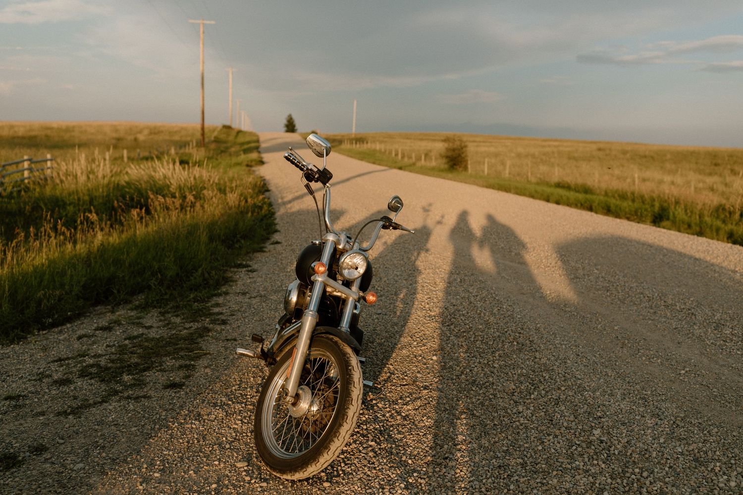 Motorcycle parked on empty country road at sunset creating long shadows.