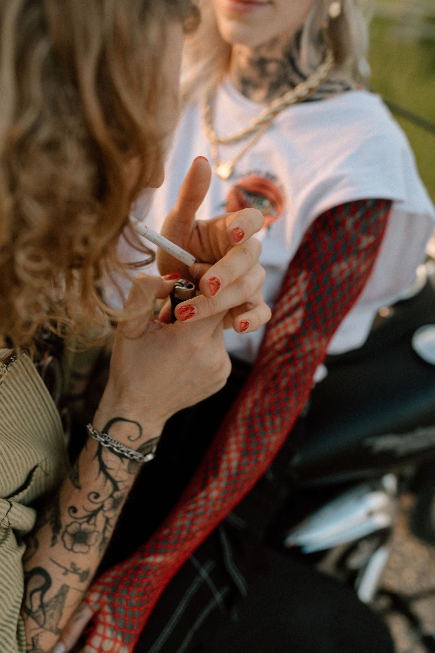 Close-up of tattooed hands with red nail polish holding a cigarette.