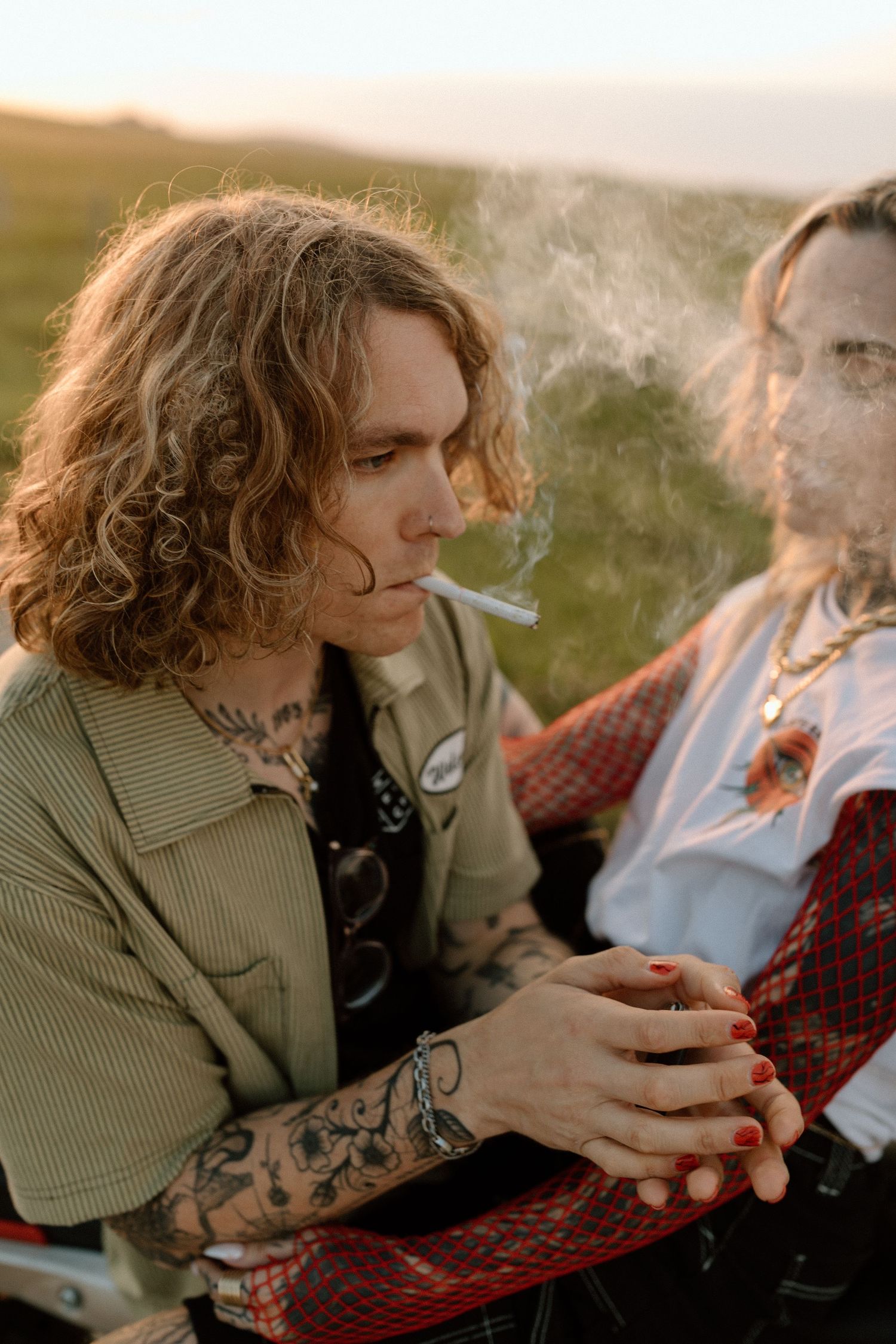 Person with curly hair smoking while sitting on motorcycle at sunset.