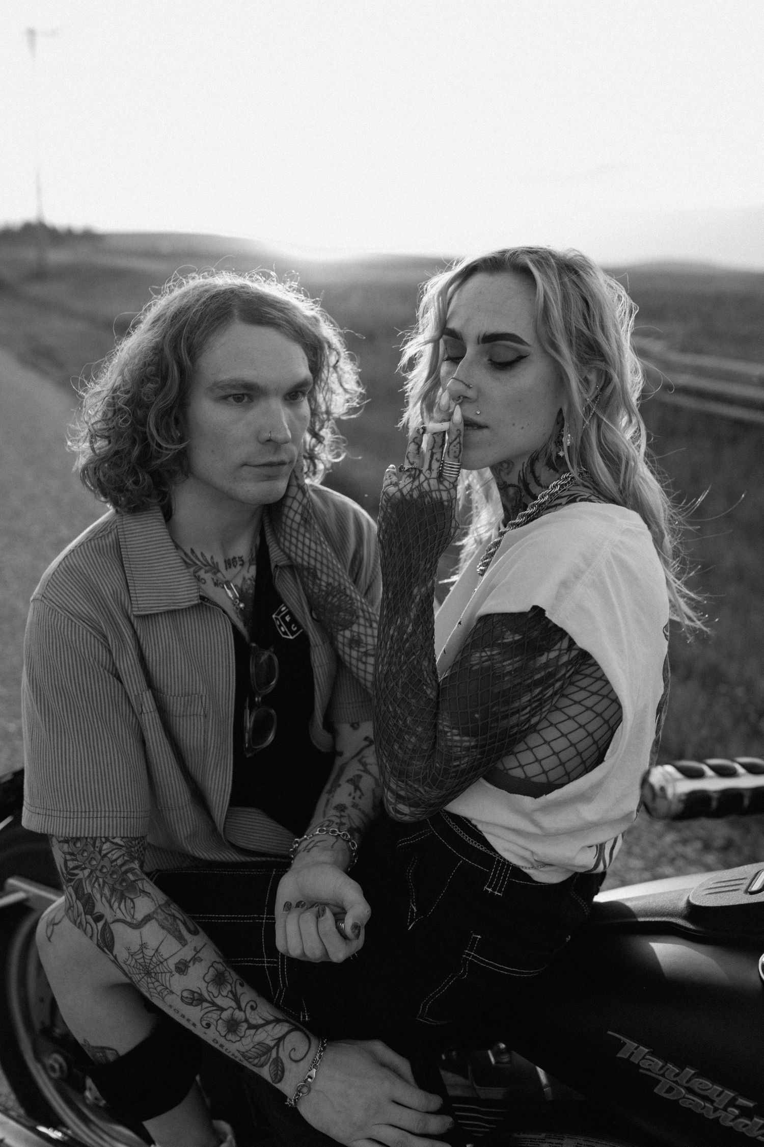 Moody black and white portrait of couple on motorcycle with dramatic lighting.