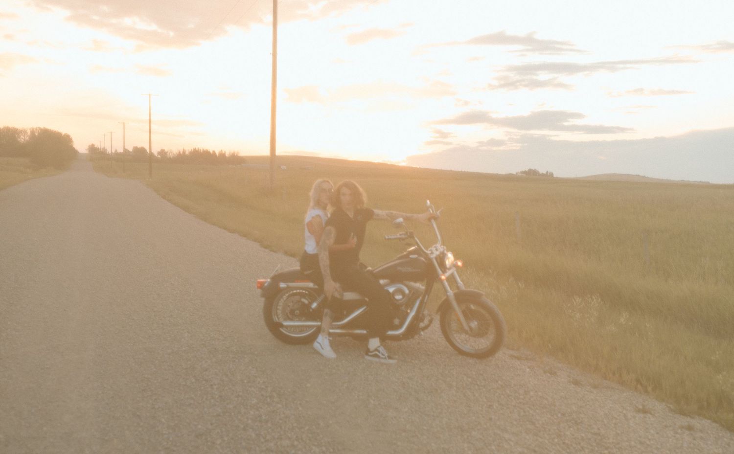 Motorcycle riders at sunset with warm golden light on country road.