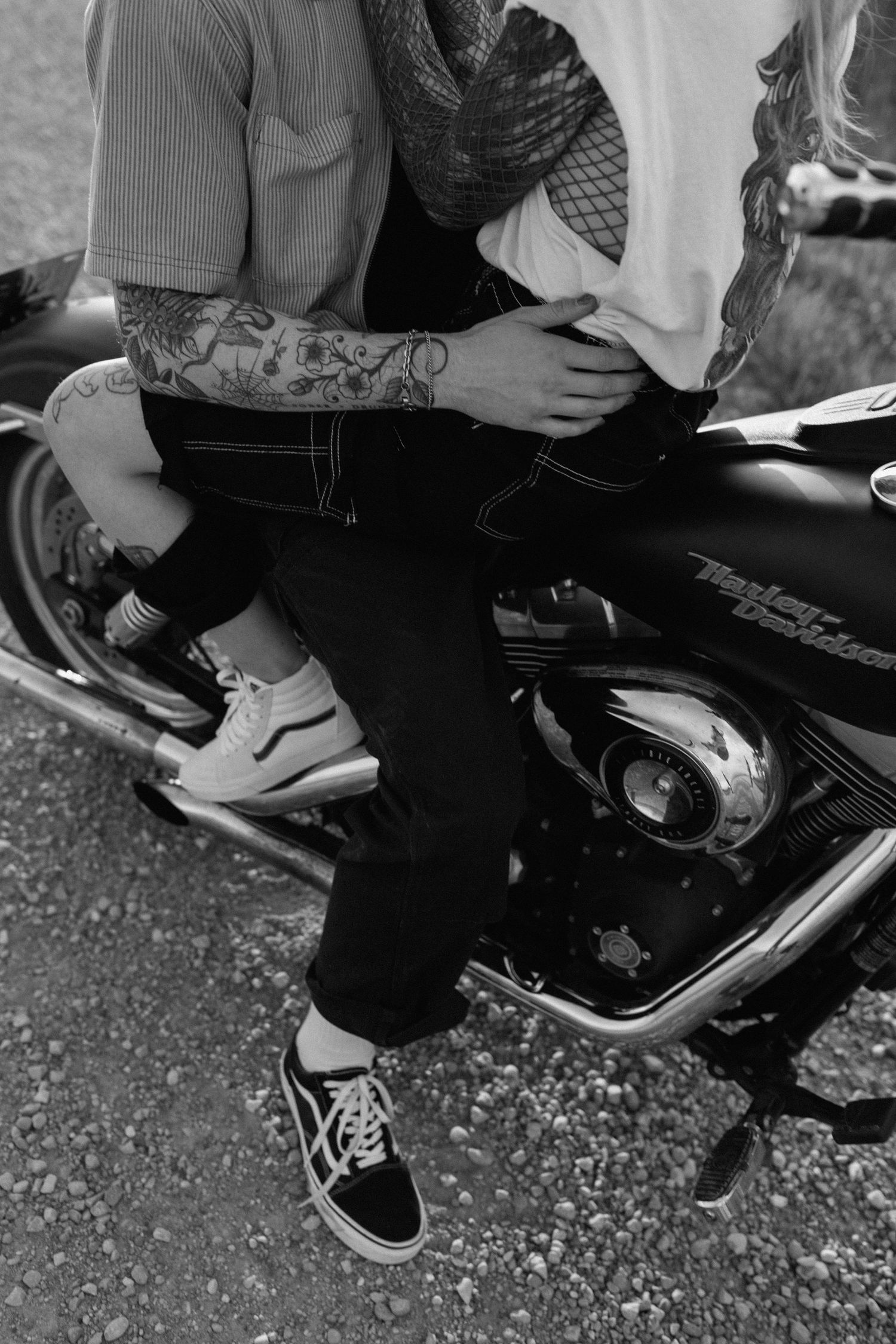 Close-up of tattooed arm and casual sneakers on motorcycle seat.
