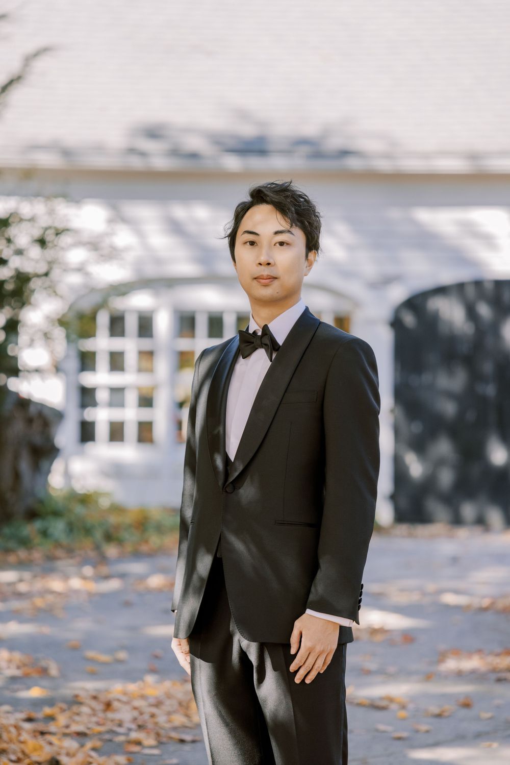A formal wedding portrait session with a black tuxedo against a light background.