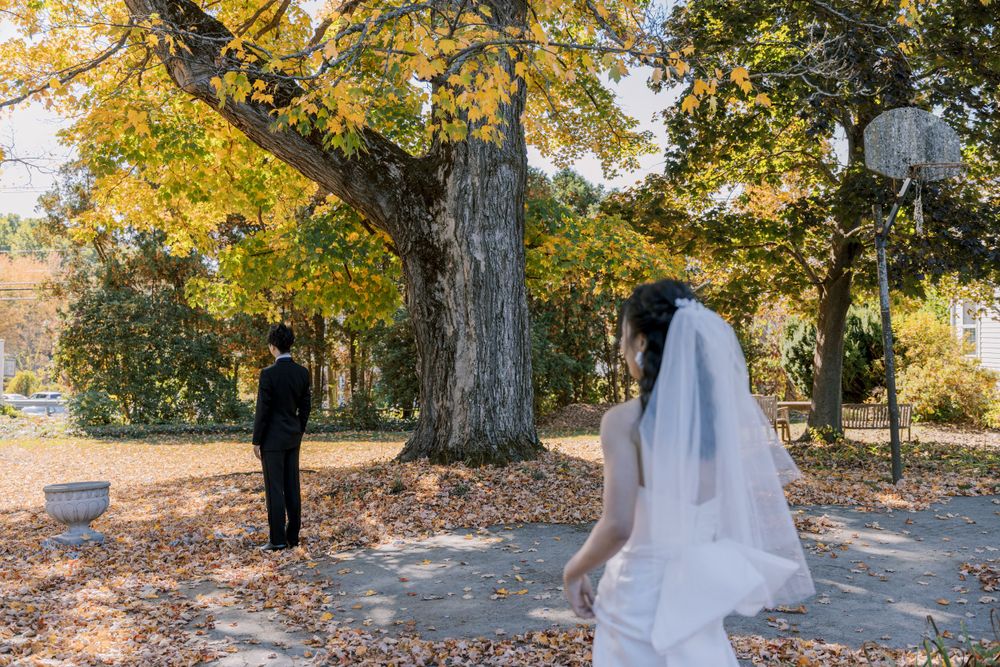 A wedding first look moment under autumn trees with fallen leaves on a beautiful sunny day.