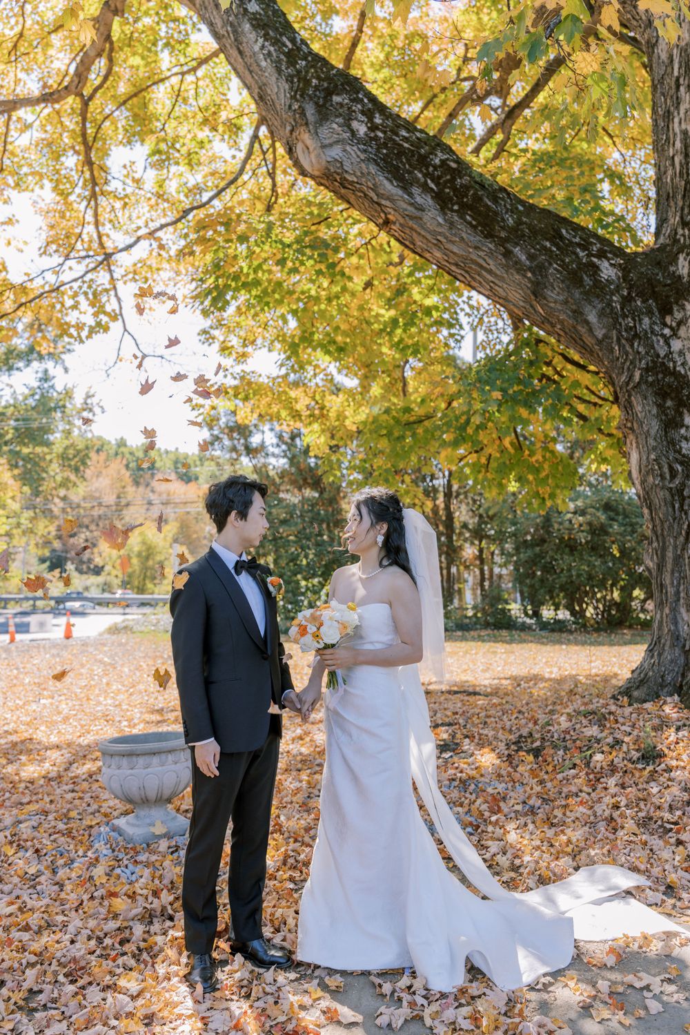 A romantic autumn wedding portrait with a couple standing beneath a massive tree with yellow leaves.