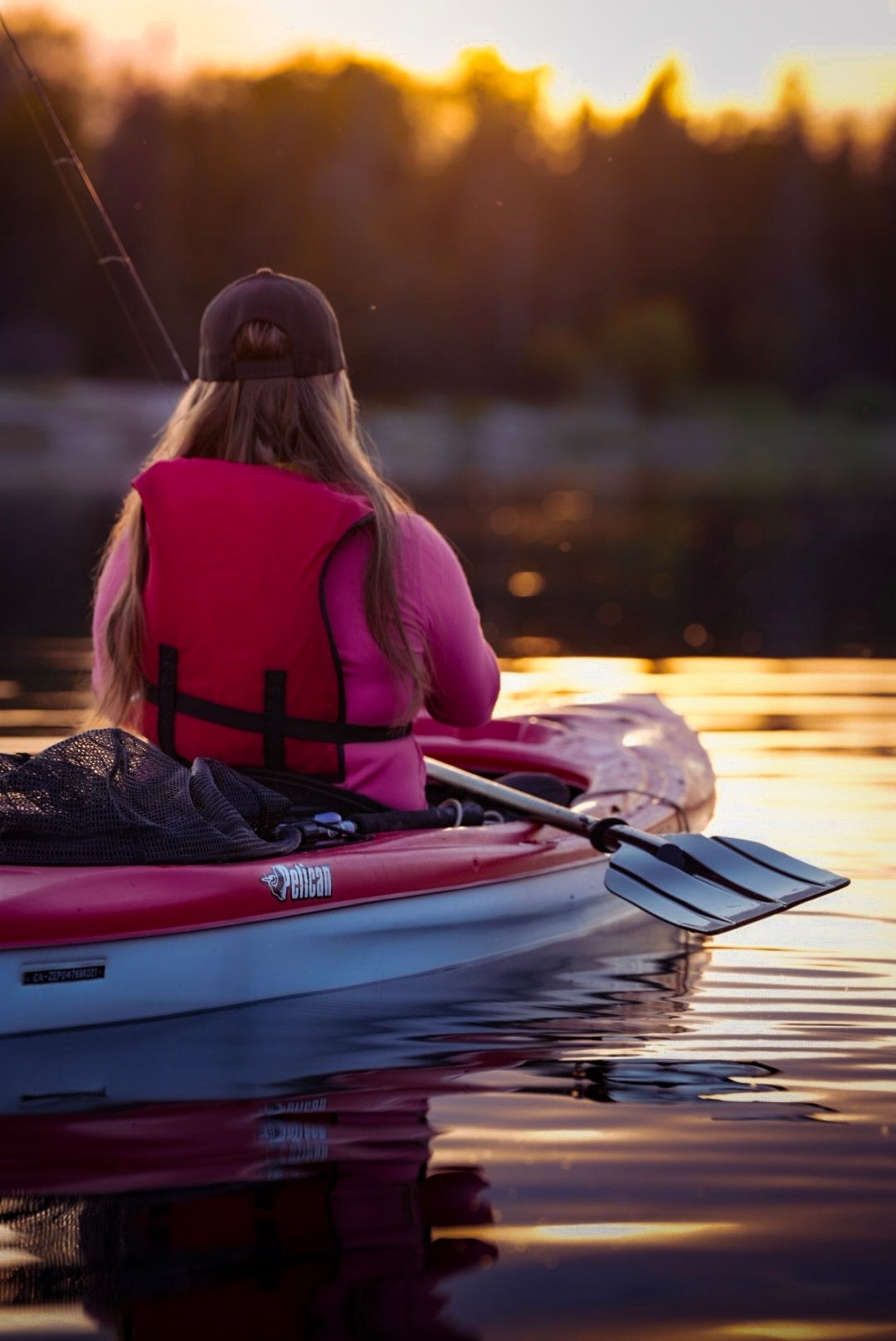 Kayaker in pink life vest paddling on calm water during golden sunset.