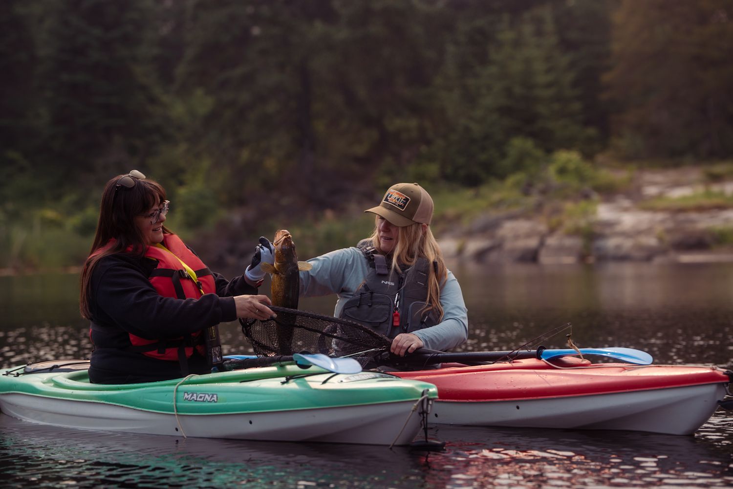 People kayaking on a serene lake surrounded by mountains and forests during a peaceful outdoor adventure.