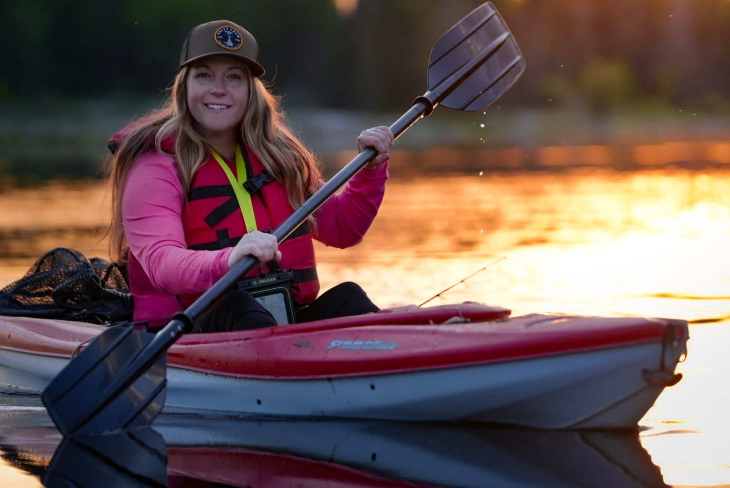 Kayaker in pink jacket holding paddle while enjoying sunset on the water.