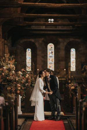 Inside Askham Hall with stained glass windows, a wedding ceremony takes place on a red carpet runner.