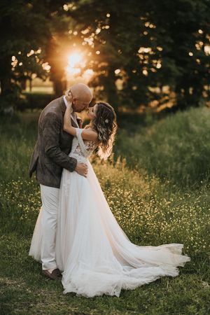 Romantic wedding couple embraces during golden hour in an international wildflower meadow with flowing white dress and dreamy lighting.