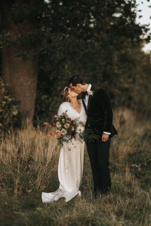 A couple shares an intimate moment in a field of tall grass during golden hour.
