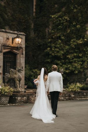 Newlyweds walk together along a stone path outside a historic building at dusk near Askham Hall.