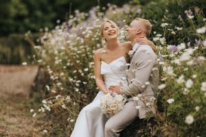 A joyful couple shares a laugh among blooming cosmos flowers at Hodsock Priory in their wedding attire.