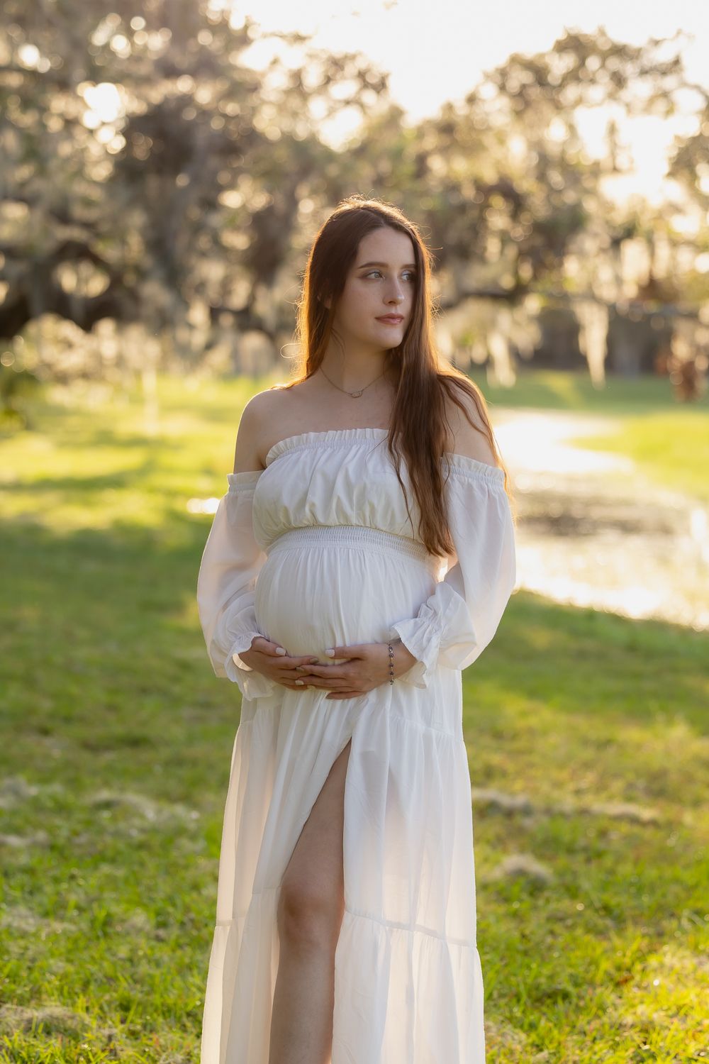 Maternity portrait of woman in white off-shoulder dress during golden hour.