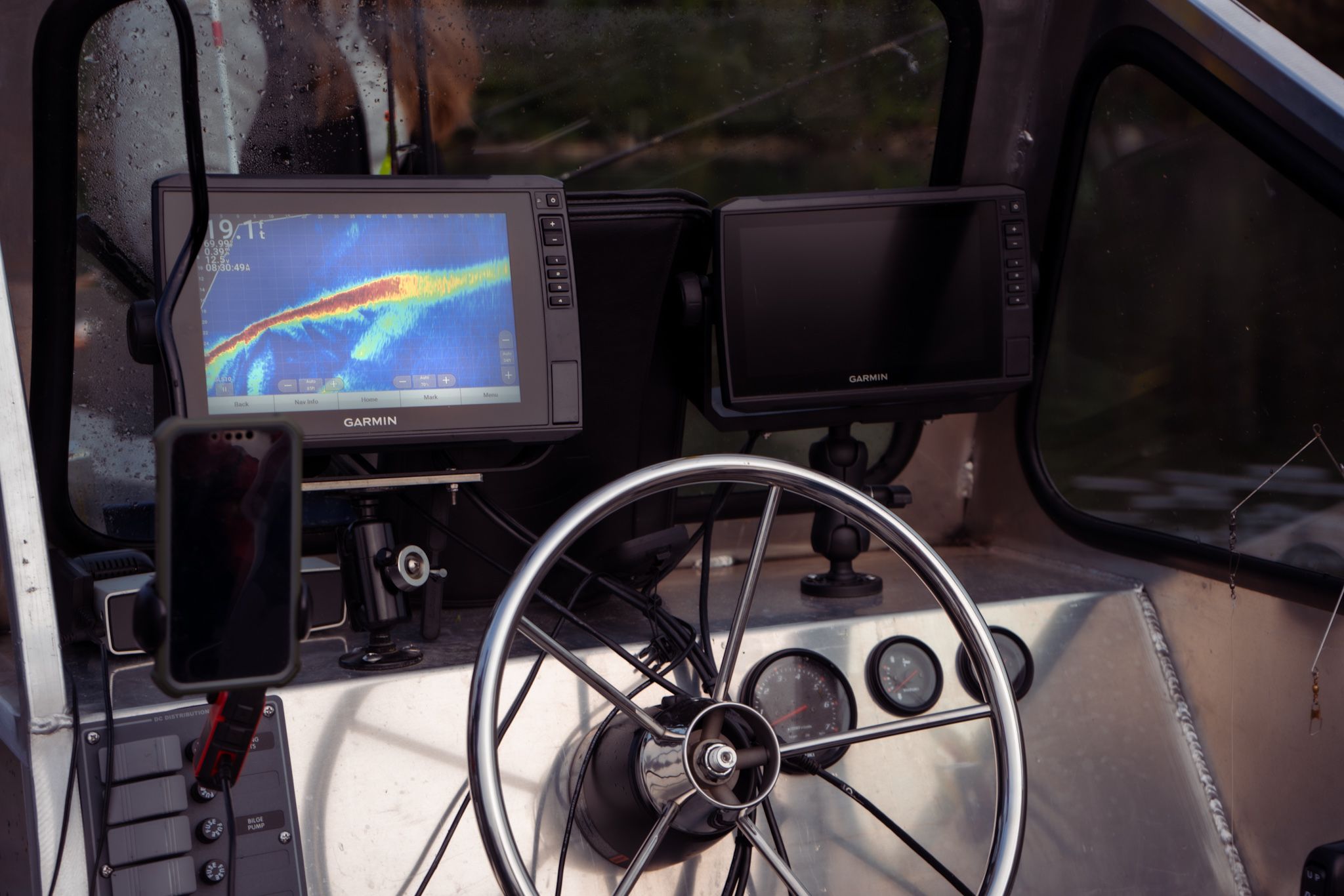 Modern boat dashboard displaying electronic navigation equipment and steering wheel.