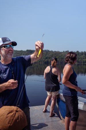 Fishing enthusiasts stand on a boat deck during a sunny day at the lake.