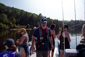 Group of people fishing together from a boat on a calm lake surrounded by trees.