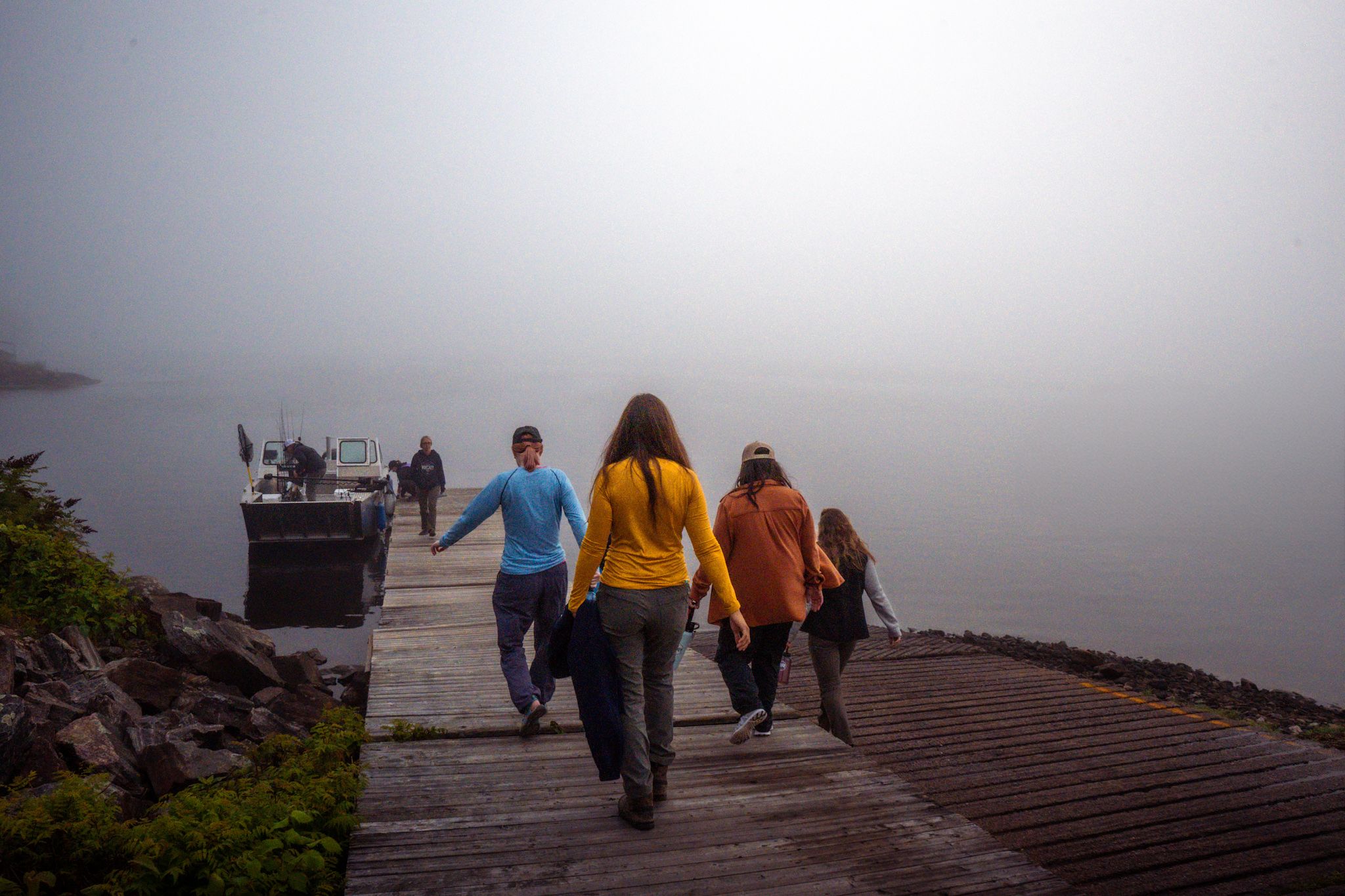 People walking on a wooden dock in foggy weather near a lake.