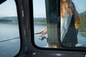 View through boat window of fishing rod and gear on calm waters.