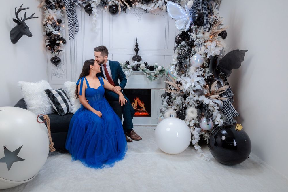 Couple poses in front of a winter wonderland backdrop with black and white balloons and silver decorations.