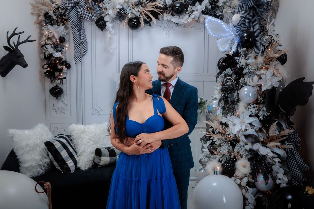 Couple in formal attire poses romantically against a decorated winter backdrop.