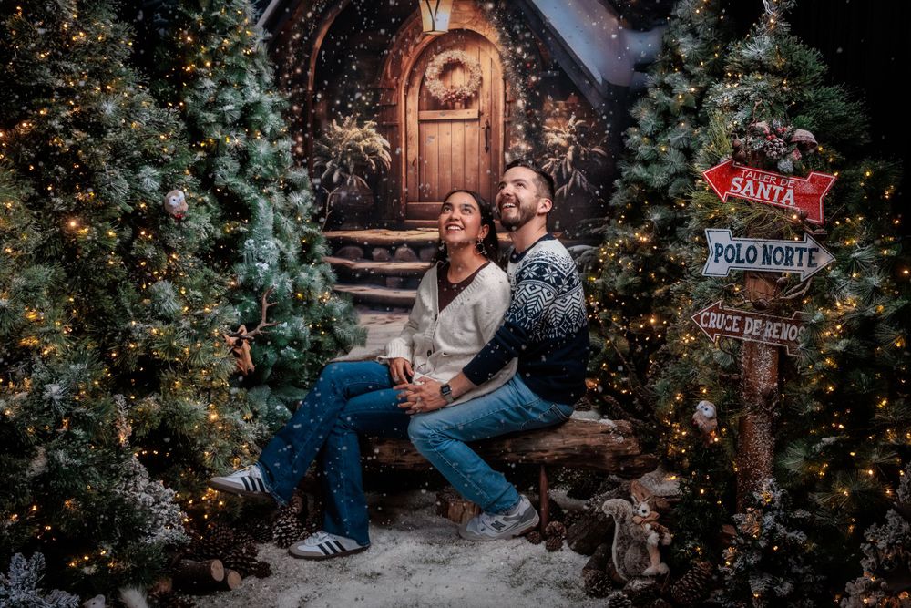Couple poses intimately among twinkling Christmas lights and festive decorations.