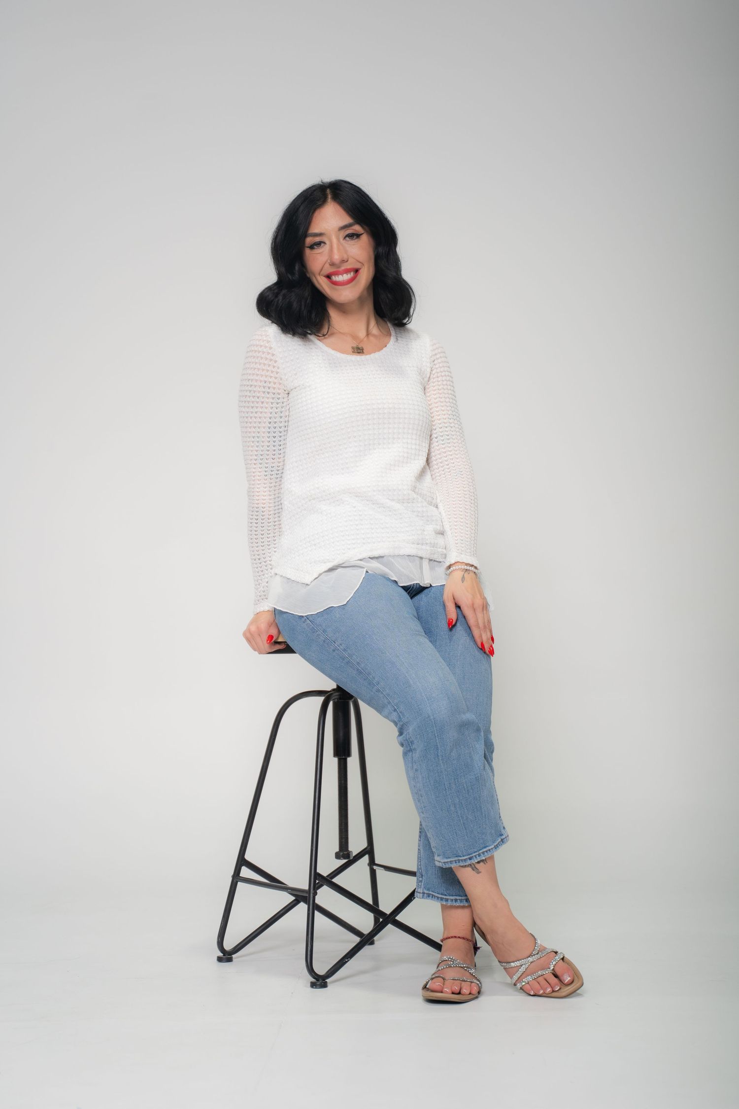 Person in black top and animal print skirt posing on wooden stool against neutral background.