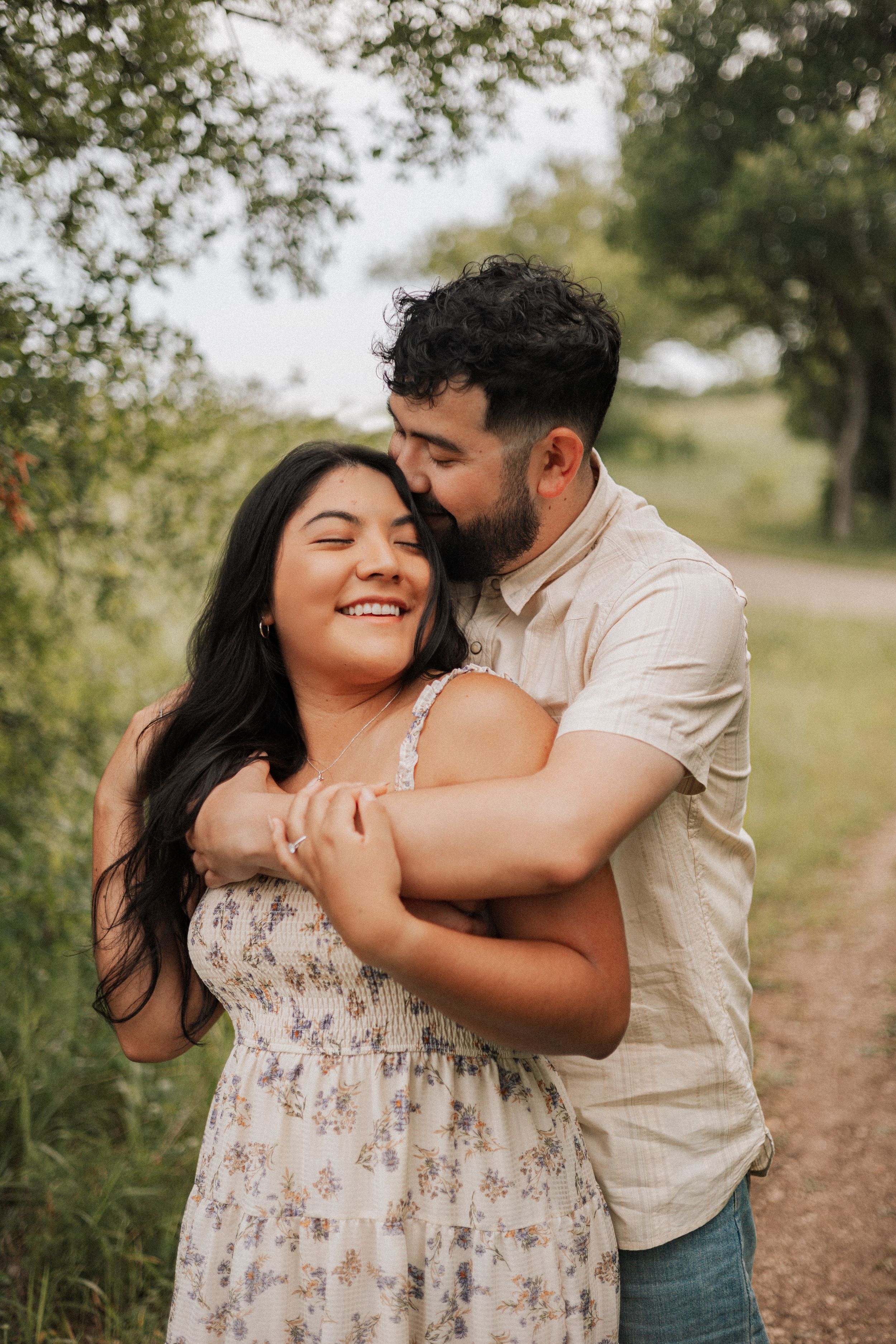 A tender romantic moment shared between a couple embracing on a sunlit dirt path surrounded by greenery.