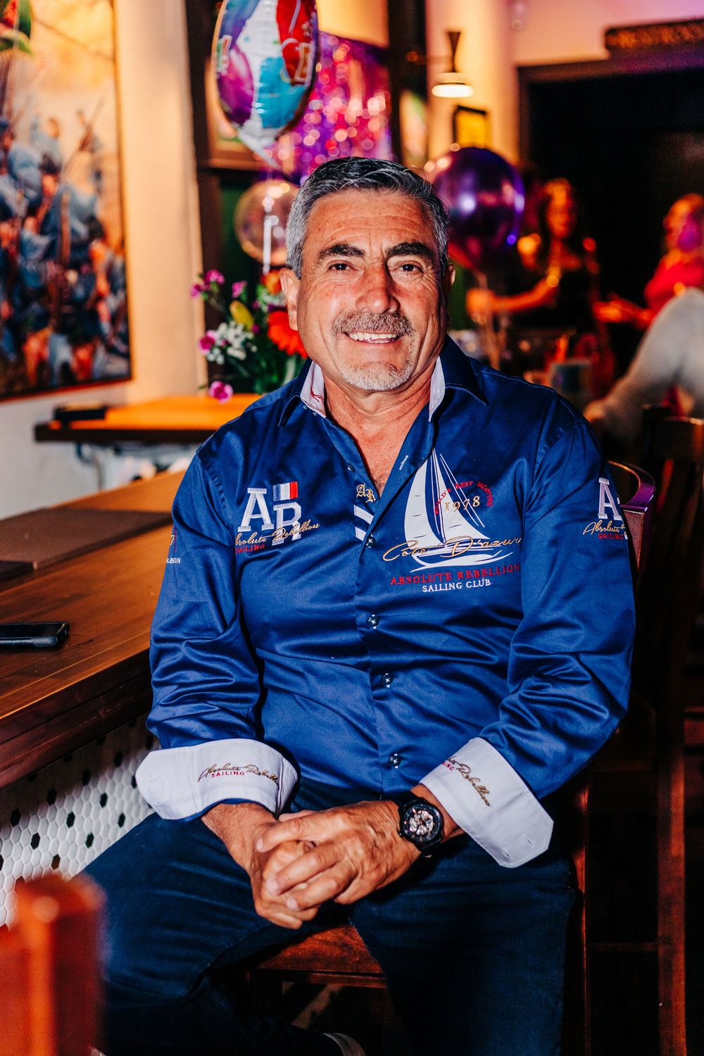 Man in blue sailing jacket smiling while seated at a bar during a celebration at an event in lake worth.