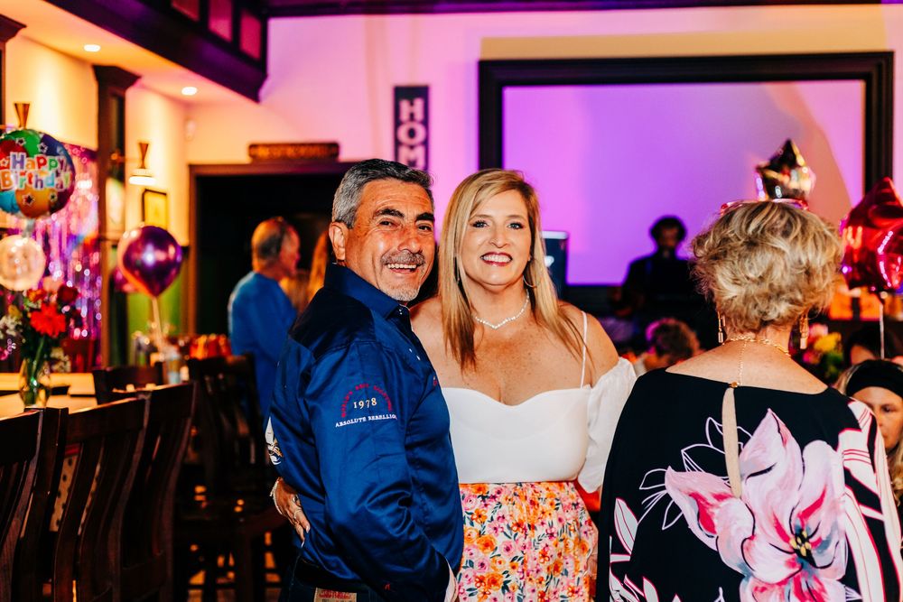 Partygoers smiling together at a bar with pink ambient lighting and decorative balloons at an event in lake worth.