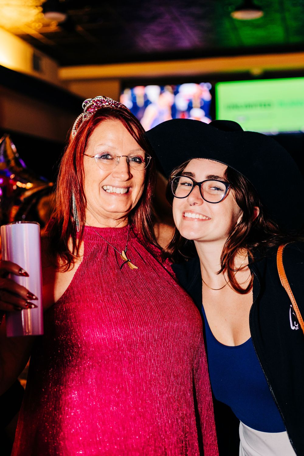 Two friends pose for photo at bar with colorful lighting and TV screens in background at an event in lake worth.