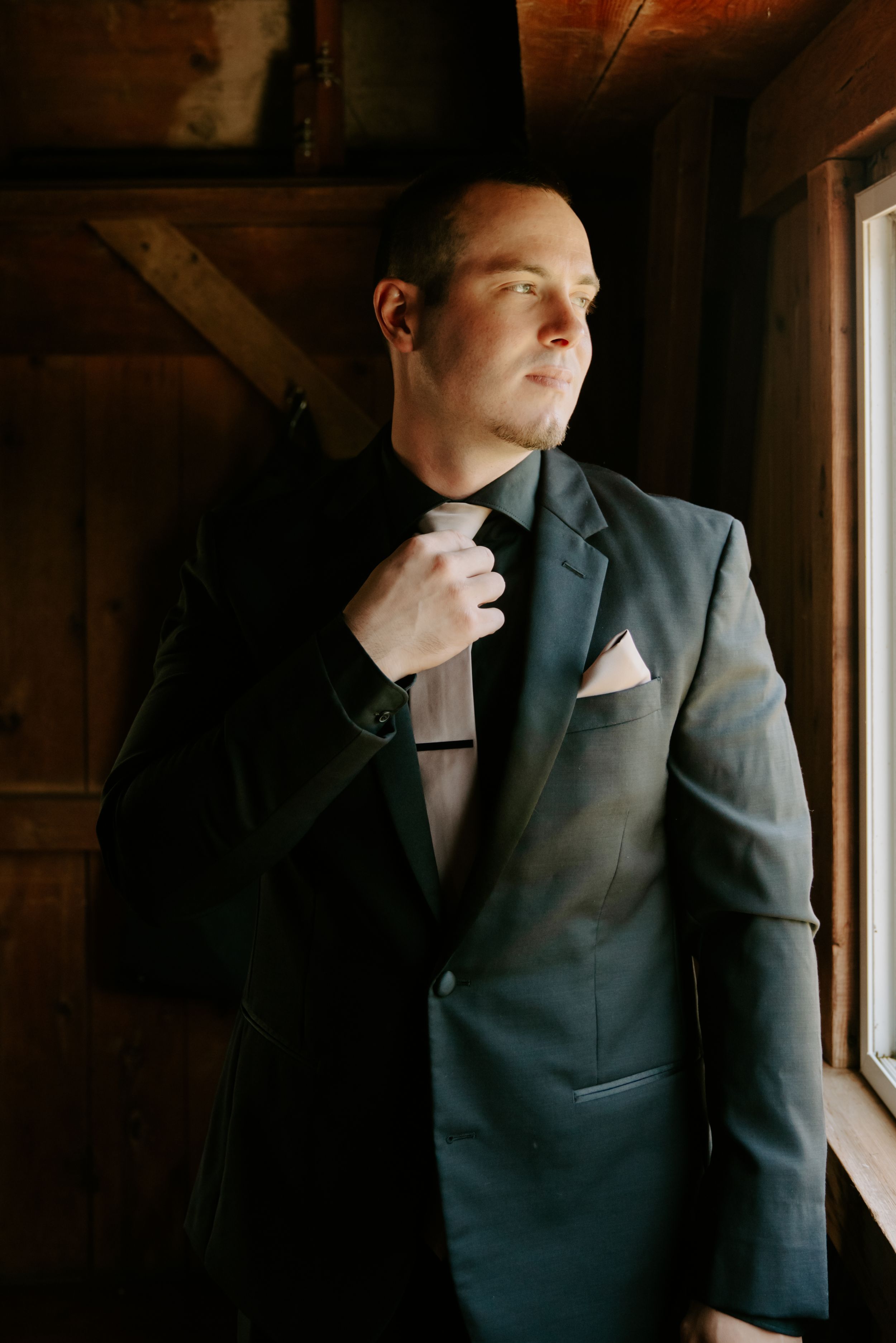 Moody portraits of a person in a dark suit looking contemplatively by a window.