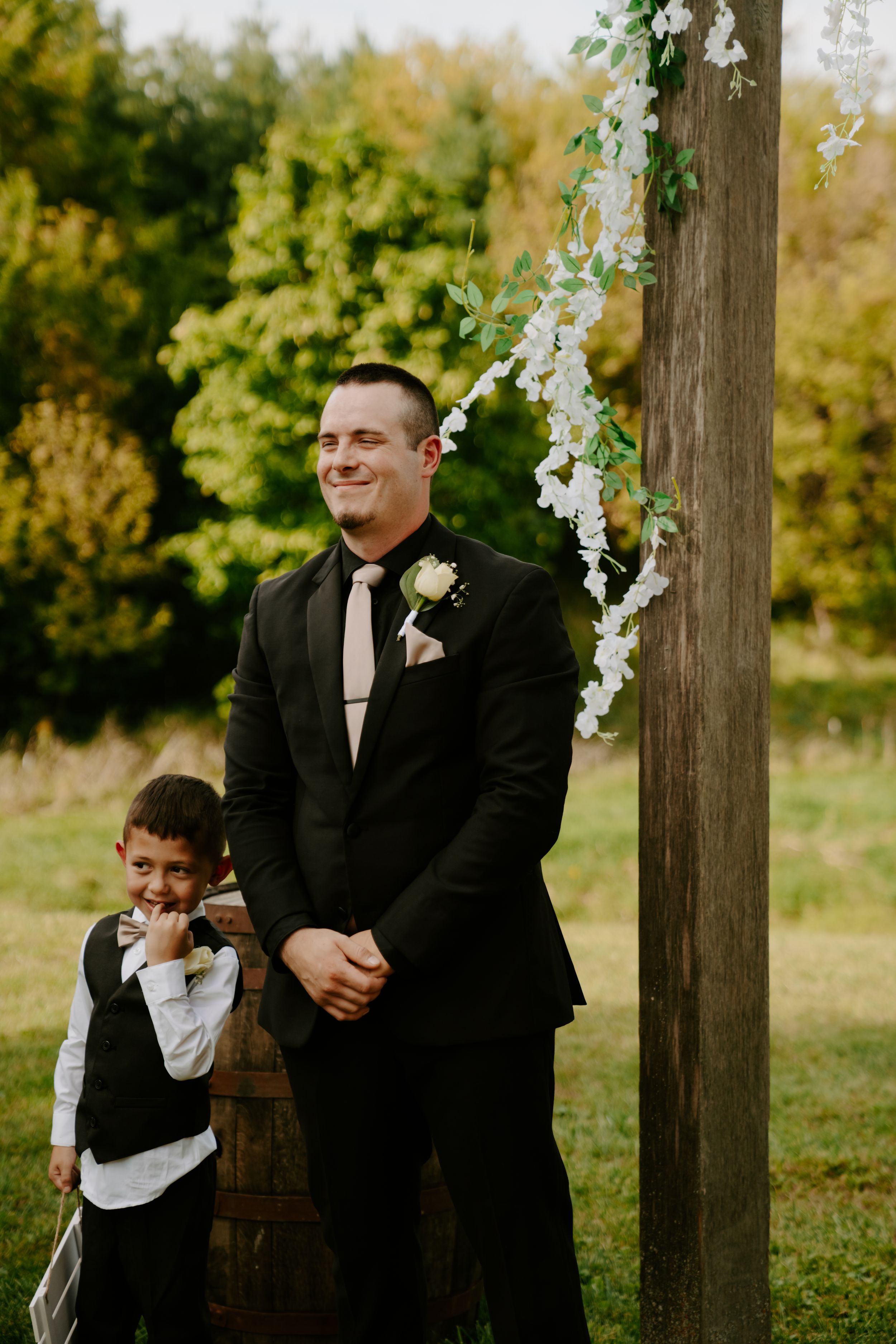 Wedding party members and children sharing candid moments by floral-decorated posts.