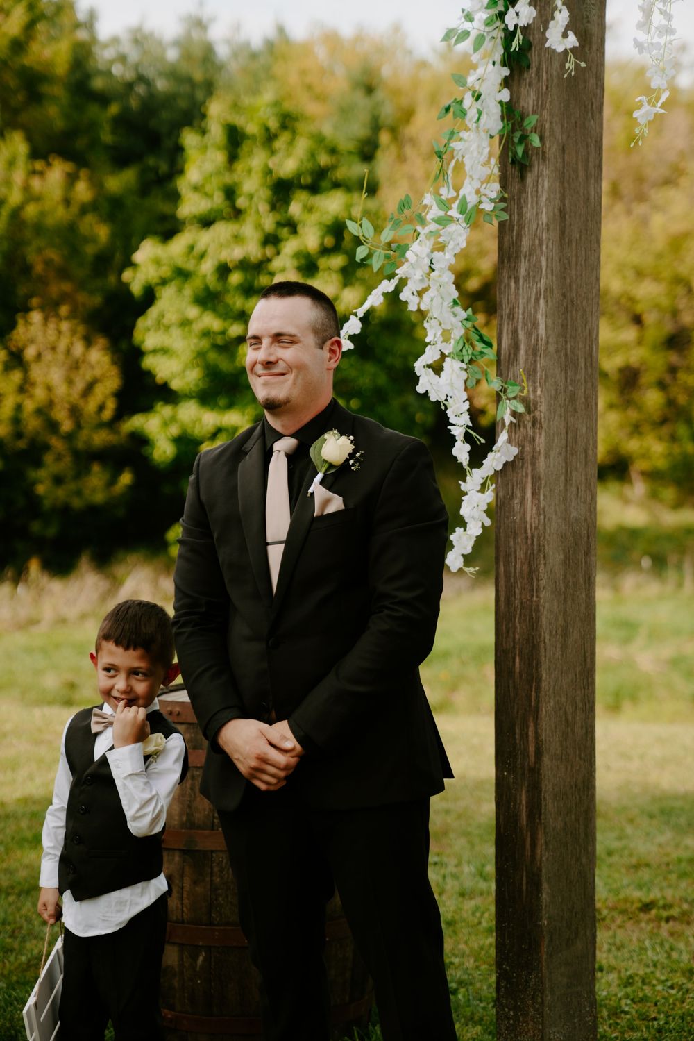 Wedding party members and children sharing candid moments by floral-decorated posts.