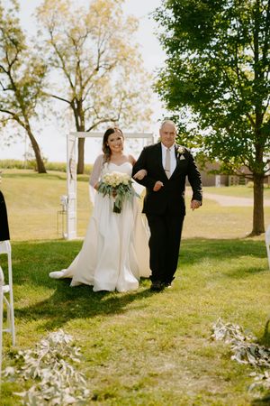 Joyful wedding processional walking through outdoor ceremony space with white floral decorations.