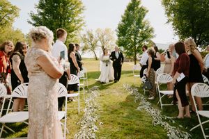 Wedding ceremony guests seated on white chairs in an outdoor garden setting during golden hour.