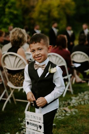 Young ring bearer in formal attire walking down aisle at outdoor wedding ceremony.