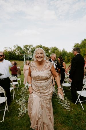 Wedding guests in formal attire gathering around white chairs at outdoor ceremony.