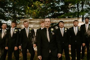 Wedding party in formal attire poses in front of stone wall during outdoor photo session.
